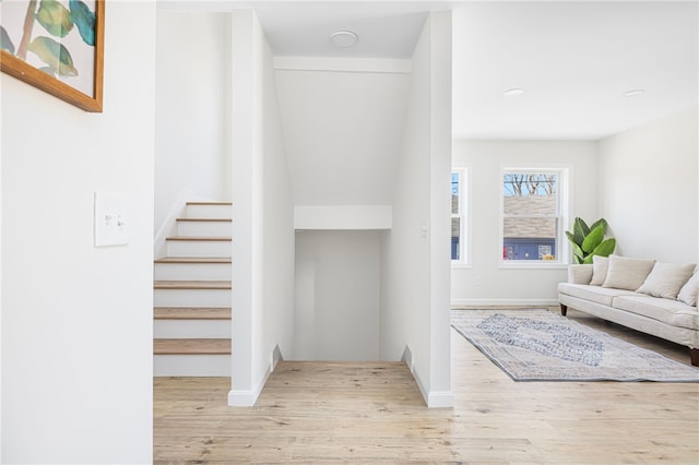 foyer entrance featuring baseboards, light wood finished floors, and stairs