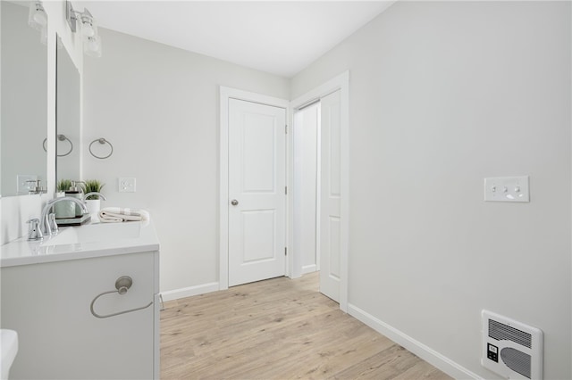 bathroom featuring baseboards, a sink, wood finished floors, and heating unit