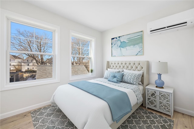 bedroom featuring light wood finished floors, baseboards, and a wall mounted AC