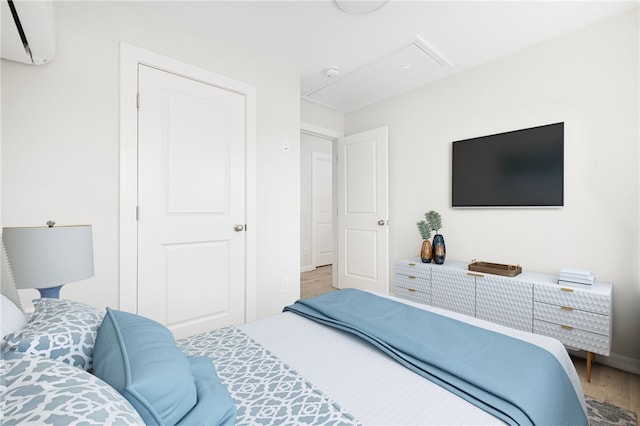 bedroom featuring a wall unit AC, wood finished floors, and attic access