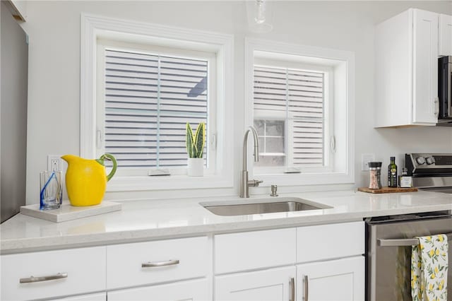 kitchen with stainless steel appliances, light stone counters, a sink, and white cabinetry