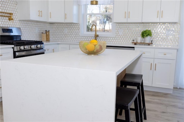 kitchen featuring a breakfast bar, white cabinetry, a center island, tasteful backsplash, and stainless steel range with gas cooktop