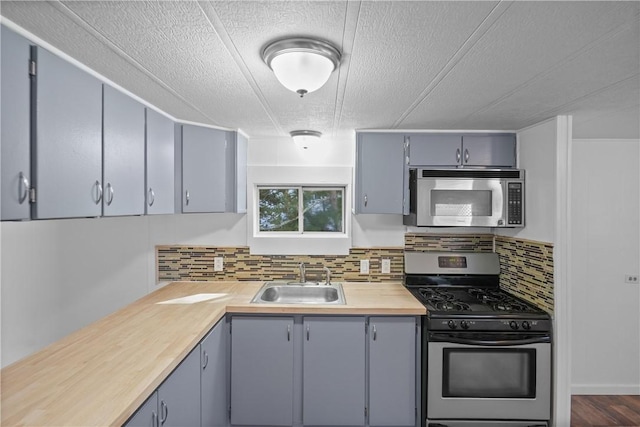 kitchen featuring sink, wooden counters, appliances with stainless steel finishes, backsplash, and a textured ceiling