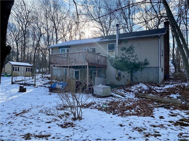 snow covered house featuring a wooden deck and a storage shed