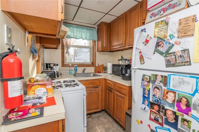 kitchen with a drop ceiling, sink, and white appliances