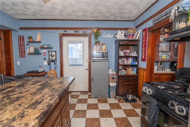 kitchen featuring ornamental molding, black gas stove, and wood walls