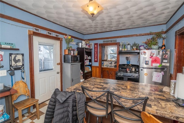 kitchen with crown molding, appliances with stainless steel finishes, dark stone counters, and wood walls