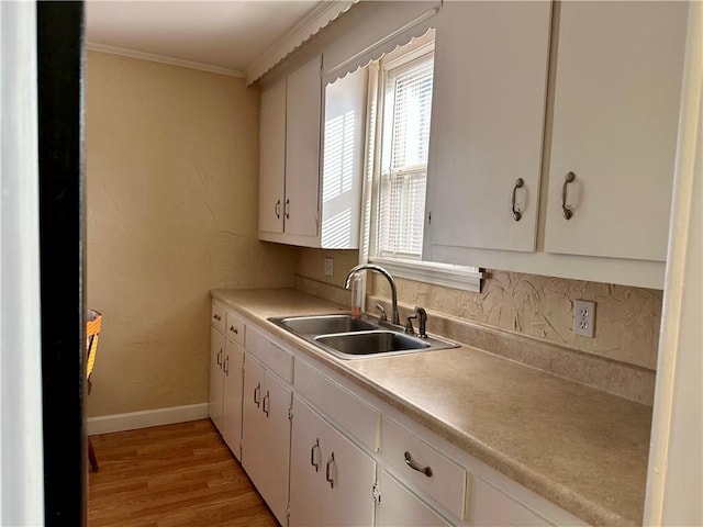 kitchen with white cabinetry, ornamental molding, sink, and light wood-type flooring