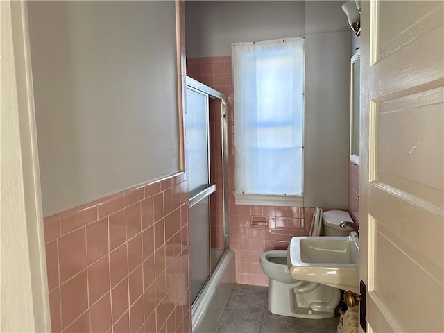 full bathroom featuring sink, tile walls, tile patterned flooring, bath / shower combo with glass door, and toilet