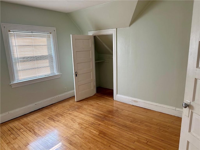 unfurnished bedroom with a closet, lofted ceiling, light hardwood / wood-style flooring, and a baseboard heating unit