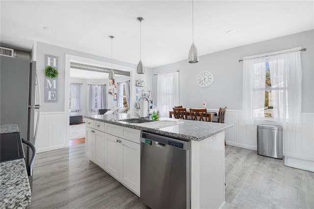 kitchen with light stone counters, hanging light fixtures, stainless steel appliances, a kitchen island with sink, and white cabinets