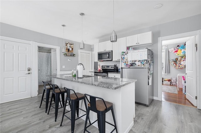 kitchen with a breakfast bar area, white cabinets, dark stone counters, hanging light fixtures, and stainless steel appliances