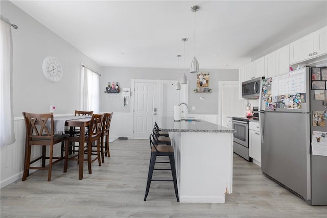 kitchen with sink, appliances with stainless steel finishes, white cabinetry, a kitchen bar, and decorative light fixtures