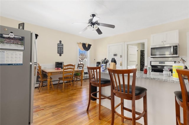 kitchen with white cabinetry, light stone counters, light wood-type flooring, appliances with stainless steel finishes, and ceiling fan