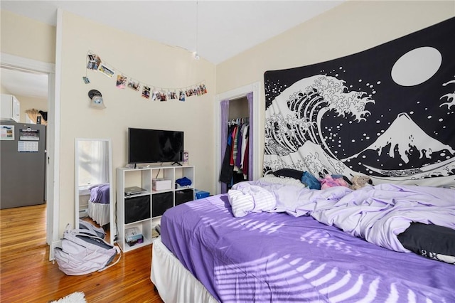 bedroom with wood-type flooring, stainless steel fridge, and a closet