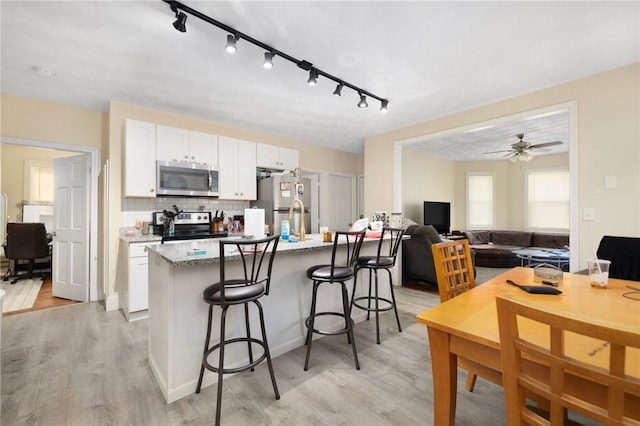 kitchen with white cabinetry, a kitchen bar, stainless steel appliances, light stone countertops, and light wood-type flooring