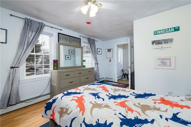 bedroom with multiple windows, ceiling fan, light wood-type flooring, and baseboard heating