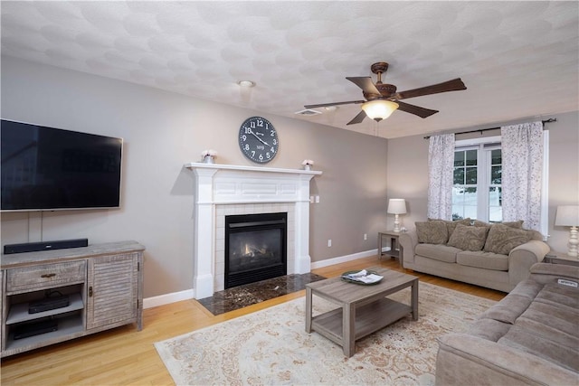 living room with ceiling fan, a fireplace, a textured ceiling, and light wood-type flooring