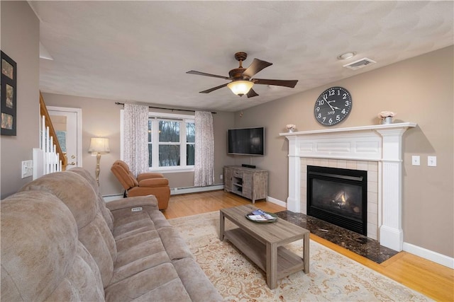 living room featuring ceiling fan, a baseboard radiator, a fireplace, and light wood-type flooring