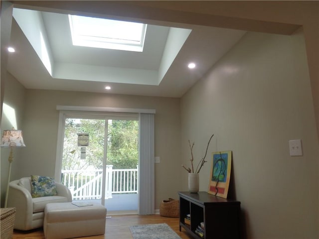 living area with a tray ceiling, a skylight, and light hardwood / wood-style floors