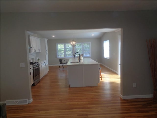 kitchen featuring white cabinetry, stainless steel gas range oven, sink, and an island with sink