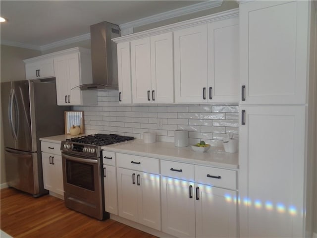 kitchen with wall chimney range hood, decorative backsplash, white cabinets, and appliances with stainless steel finishes