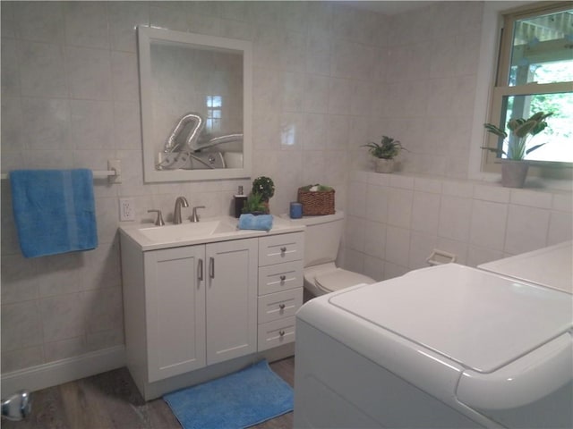 bathroom featuring toilet, tasteful backsplash, tile walls, vanity, and hardwood / wood-style floors