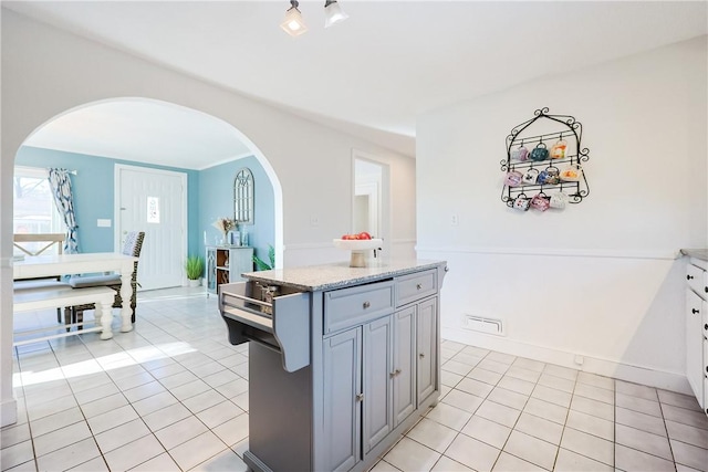 kitchen featuring light stone countertops, light tile patterned floors, a kitchen island, and gray cabinetry