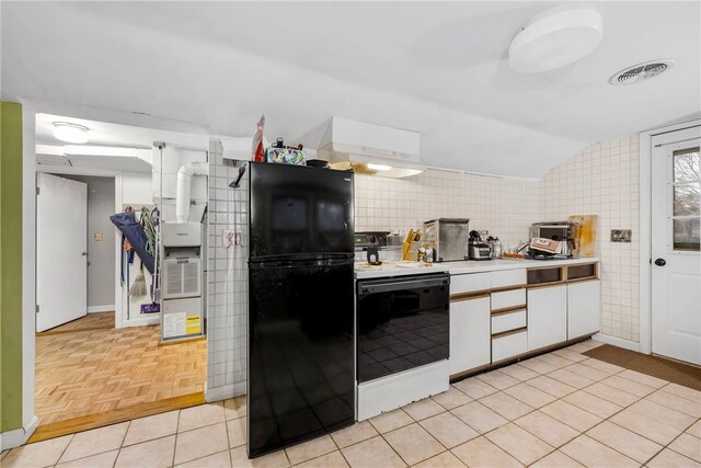 kitchen featuring light tile patterned floors, electric range, white cabinets, black fridge, and vaulted ceiling