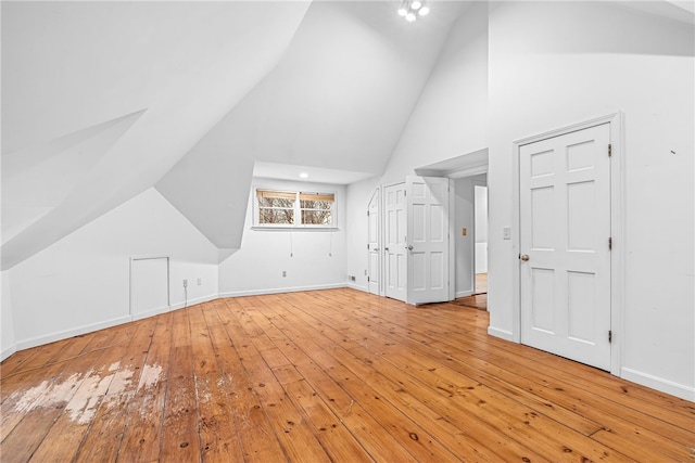 additional living space featuring high vaulted ceiling, light wood-style flooring, and baseboards