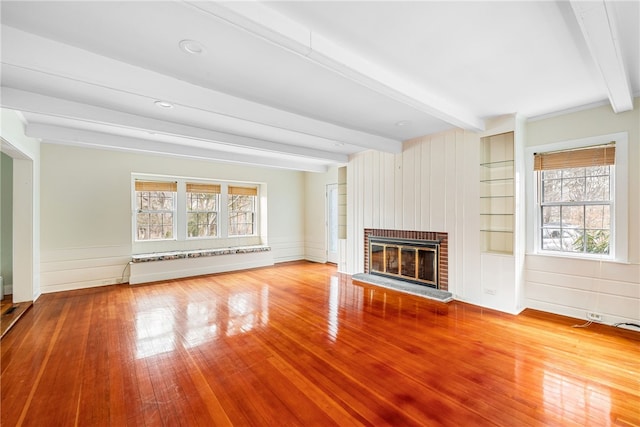 unfurnished living room featuring beamed ceiling, a brick fireplace, and hardwood / wood-style flooring