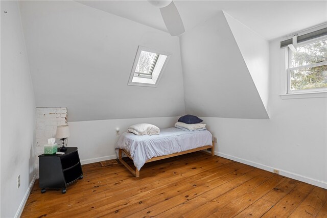 bedroom with ceiling fan, vaulted ceiling with skylight, hardwood / wood-style floors, and multiple windows