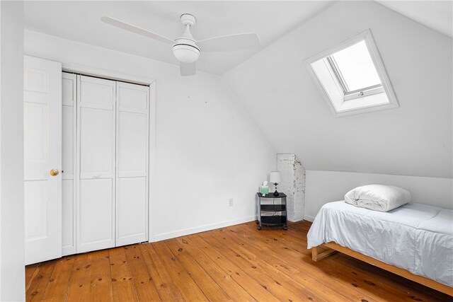 bedroom featuring a closet, lofted ceiling with skylight, a ceiling fan, light wood-type flooring, and baseboards