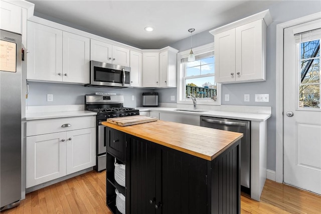 kitchen featuring a kitchen island, appliances with stainless steel finishes, wood counters, decorative light fixtures, and sink