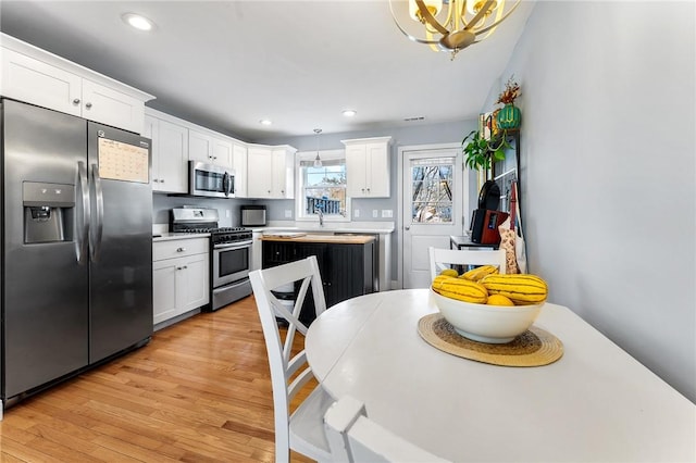 kitchen featuring white cabinetry, stainless steel appliances, decorative light fixtures, and light hardwood / wood-style flooring