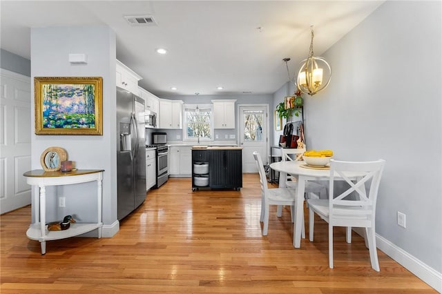 kitchen featuring appliances with stainless steel finishes, decorative light fixtures, white cabinetry, a center island, and light hardwood / wood-style flooring