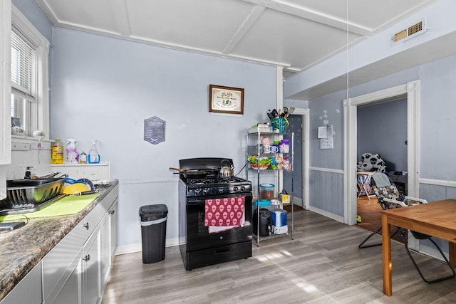 kitchen featuring white cabinetry, black range with gas stovetop, light stone countertops, and light wood-type flooring