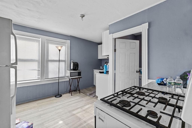 kitchen with white cabinetry, light hardwood / wood-style floors, stainless steel refrigerator, and gas range gas stove