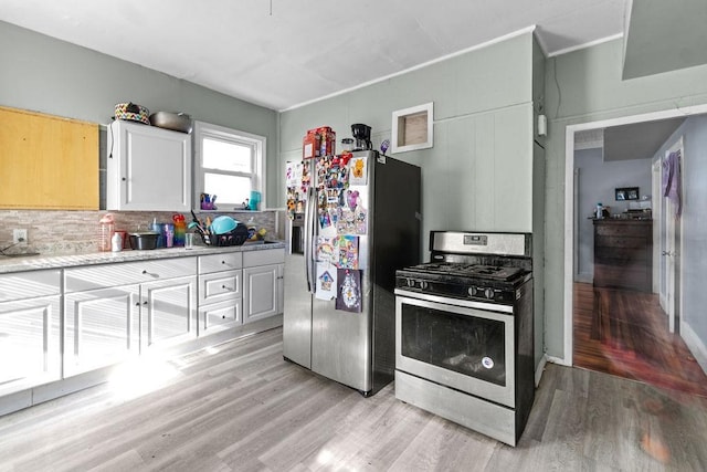 kitchen featuring appliances with stainless steel finishes, white cabinets, light hardwood / wood-style floors, and decorative backsplash