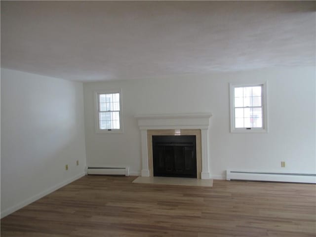 unfurnished living room with plenty of natural light, wood-type flooring, and a baseboard heating unit