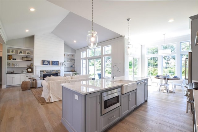 kitchen featuring sink, gray cabinets, appliances with stainless steel finishes, light stone countertops, and a center island with sink