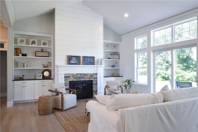 living room with built in shelves, a stone fireplace, high vaulted ceiling, and light wood-type flooring