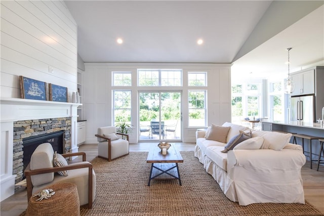 living room featuring hardwood / wood-style flooring, a stone fireplace, and high vaulted ceiling