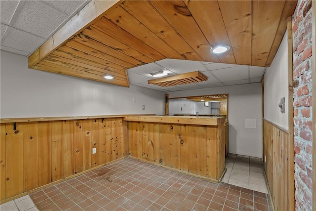 kitchen featuring a paneled ceiling, kitchen peninsula, and wood walls