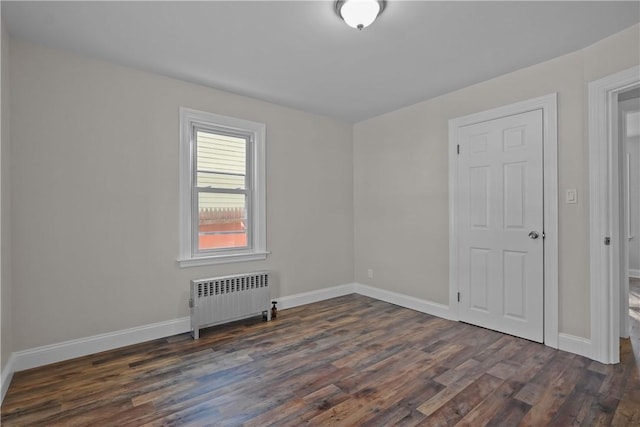 empty room with radiator heating unit and dark hardwood / wood-style flooring