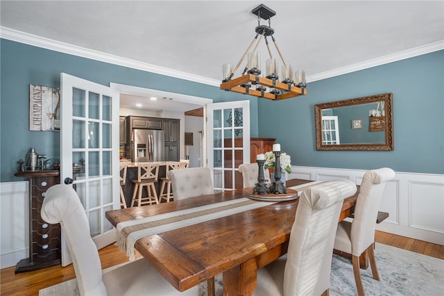 dining space with french doors, ornamental molding, light hardwood / wood-style flooring, and a notable chandelier