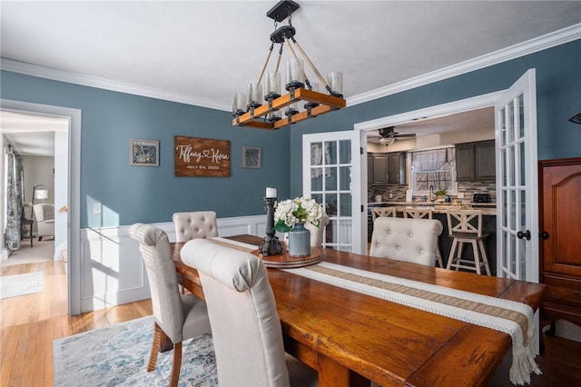 dining space featuring ornamental molding, ceiling fan with notable chandelier, and light wood-type flooring