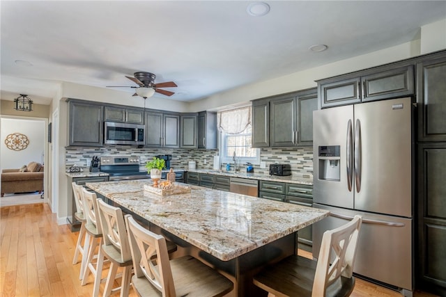 kitchen featuring a breakfast bar area, stainless steel appliances, a center island, tasteful backsplash, and light stone countertops