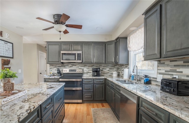 kitchen with stainless steel appliances, light hardwood / wood-style floors, sink, and light stone countertops