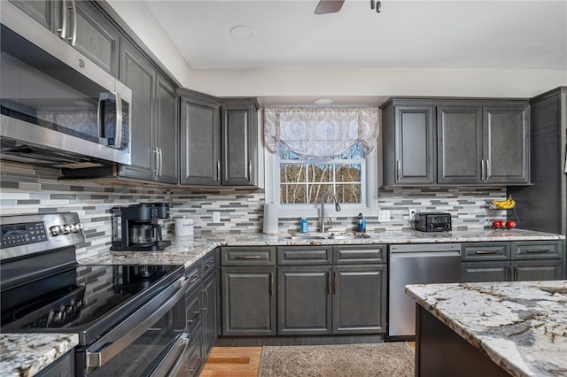 kitchen featuring sink, ceiling fan, appliances with stainless steel finishes, backsplash, and light stone countertops